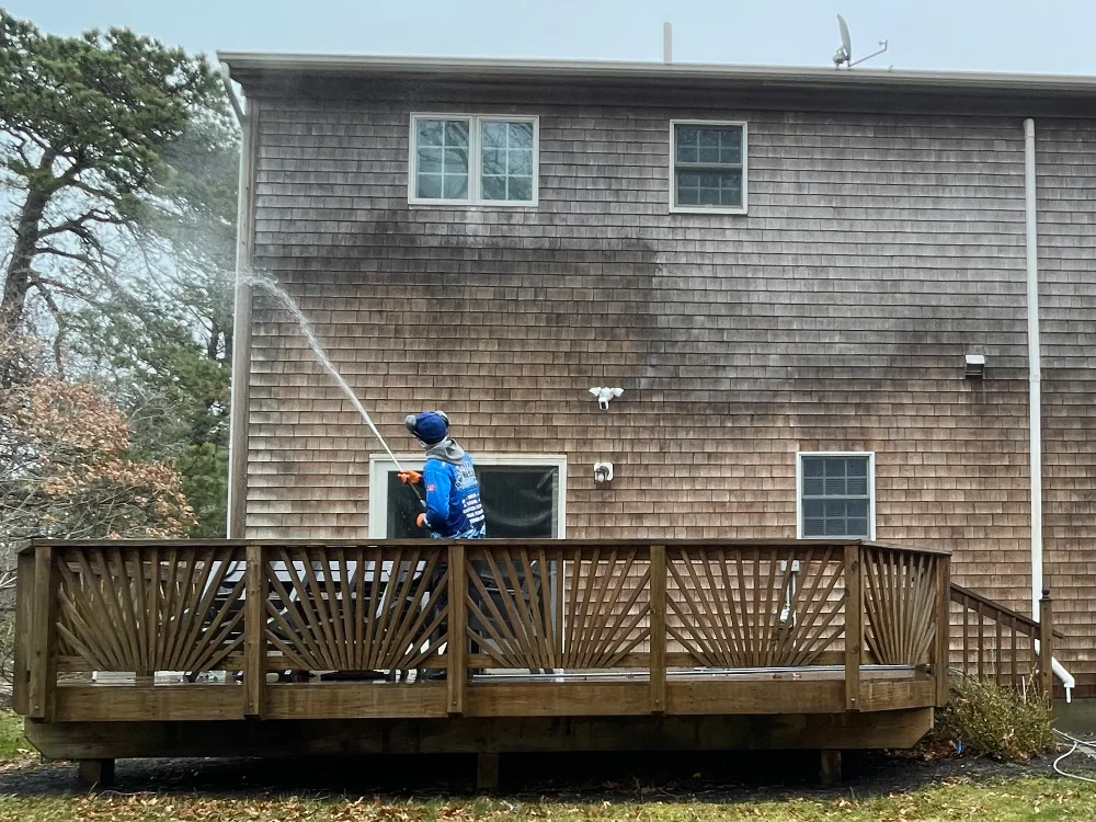 A professional power washing technician cleaning the siding of a coastal home with a low-pressure nozzle.
